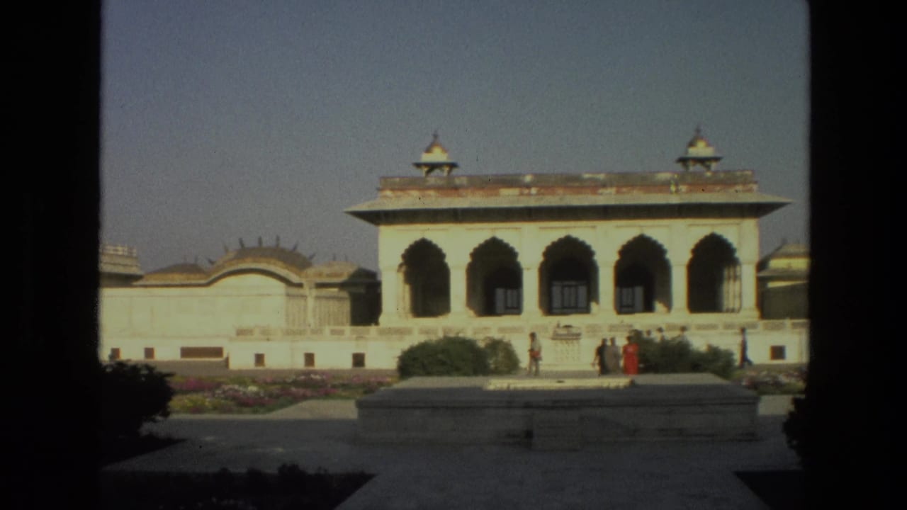 1974 India home-movie view of a white palace-style building with arched bays, low gardens, paths, and visitors near the entrance.