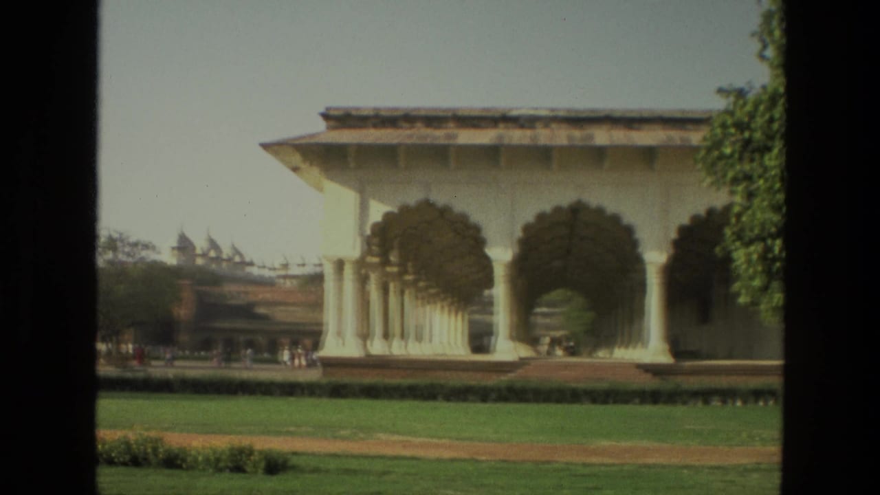 Arched colonnade beside a green lawn with distant visitors and trees.