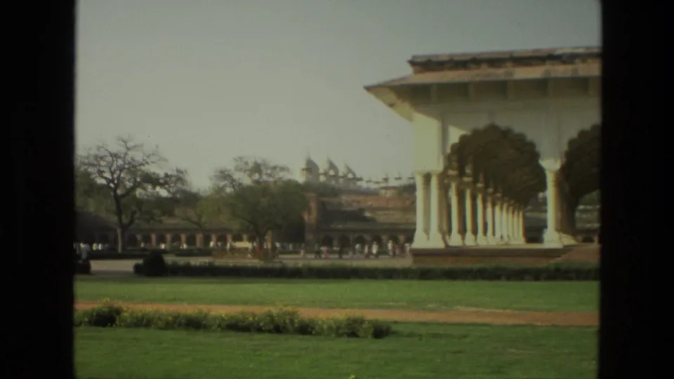 1974 India 8mm frame with the arched building cropped at right, lawn and path in front, and visitors near the far wall.