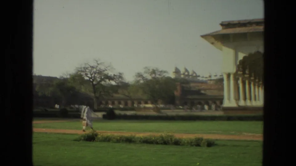 1974 India 8mm frame showing a man in light clothing walking across landscaped grounds near the arched colonnade.