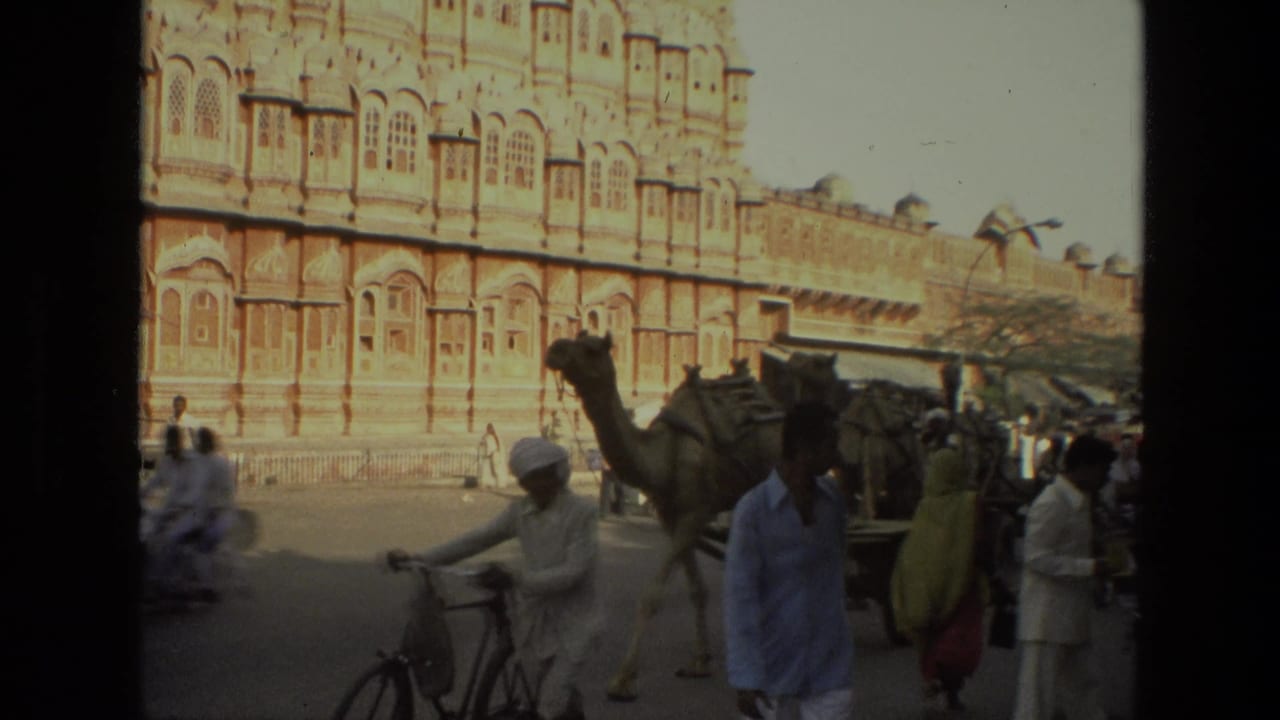 Camel cart, pedestrians, and bicycles pass in front of an ornate palace facade.