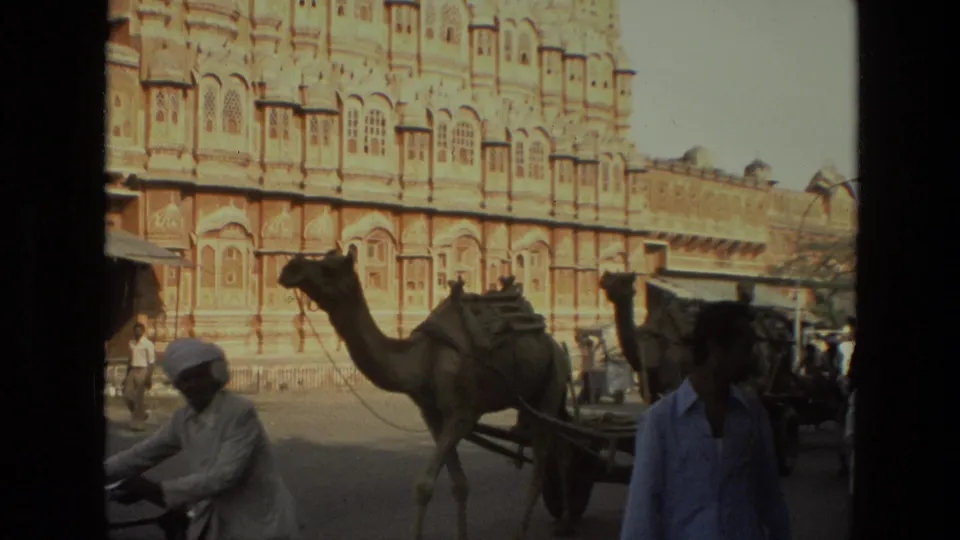 A camel-drawn cart and pedestrians move along a busy 1974 India street in front of Hawa Mahal.