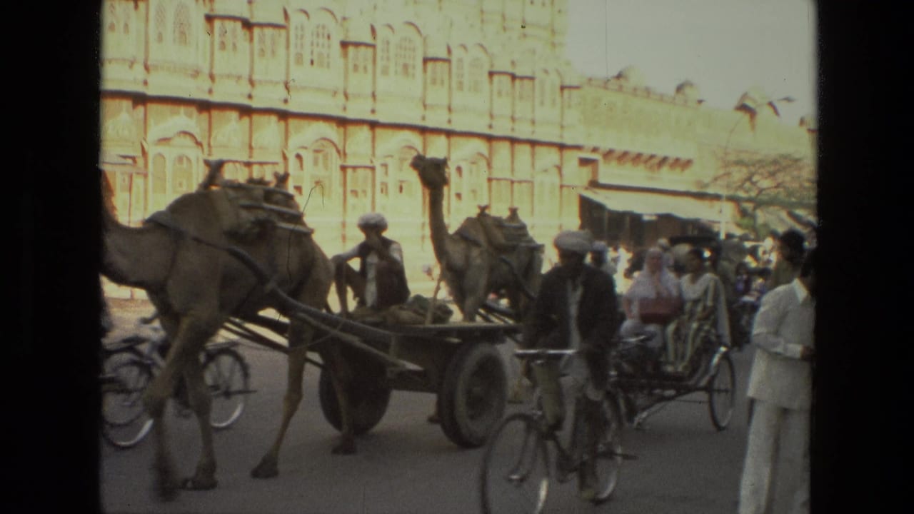 Camel cart and bicycles pass in front of a large ornate building on a crowded street.