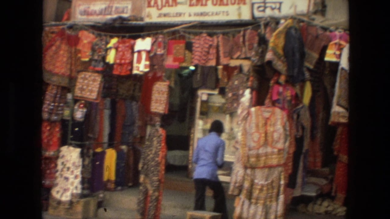Market stall with colorful garments hanging around a woman in a blue top.
