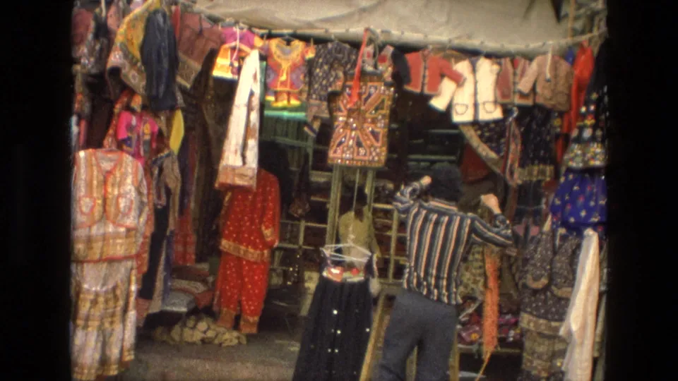 1974 India 8mm frame filled with traditional garments, patterned fabrics, and market display racks.
