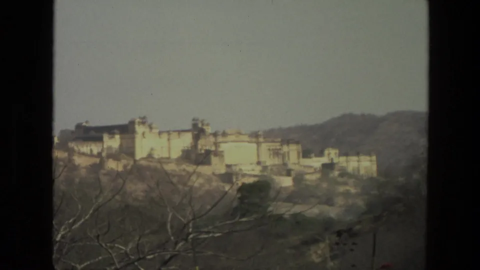 1974 India travel-film frame showing a pale hilltop palace or fortress complex across a dry hillside landscape.