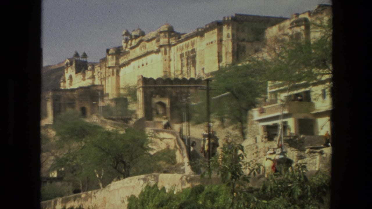 Sunlit historic hillside building with arched entrance, trees, stone walls, and pedestrians below.
