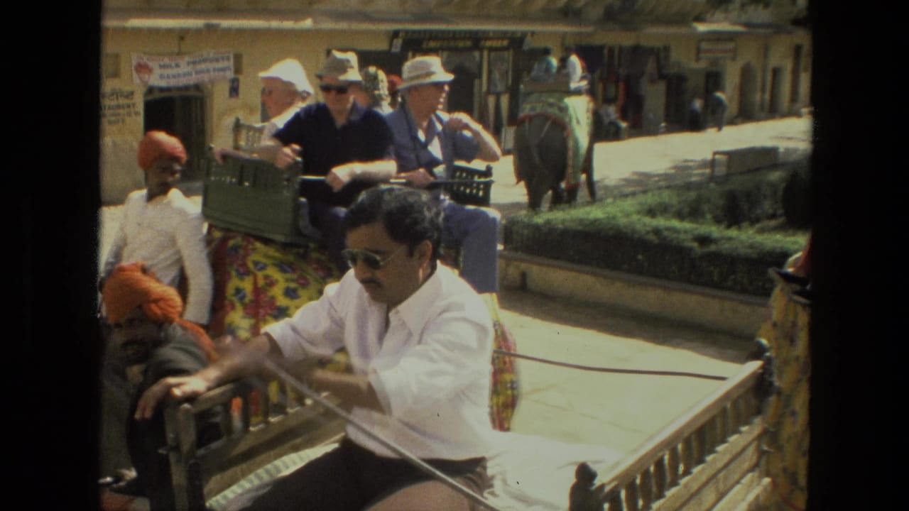 Men ride a decorated elephant while a man in sunglasses steers a cart nearby.