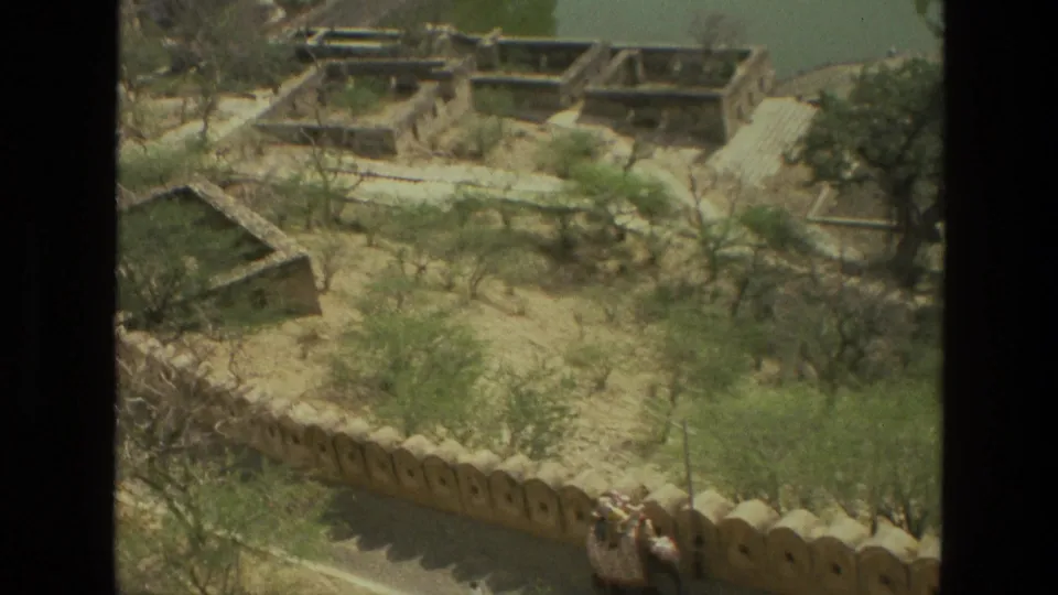 1974 8mm view over an Indian walled historic landscape with dry gardens, scattered trees, paths, and buildings near water.