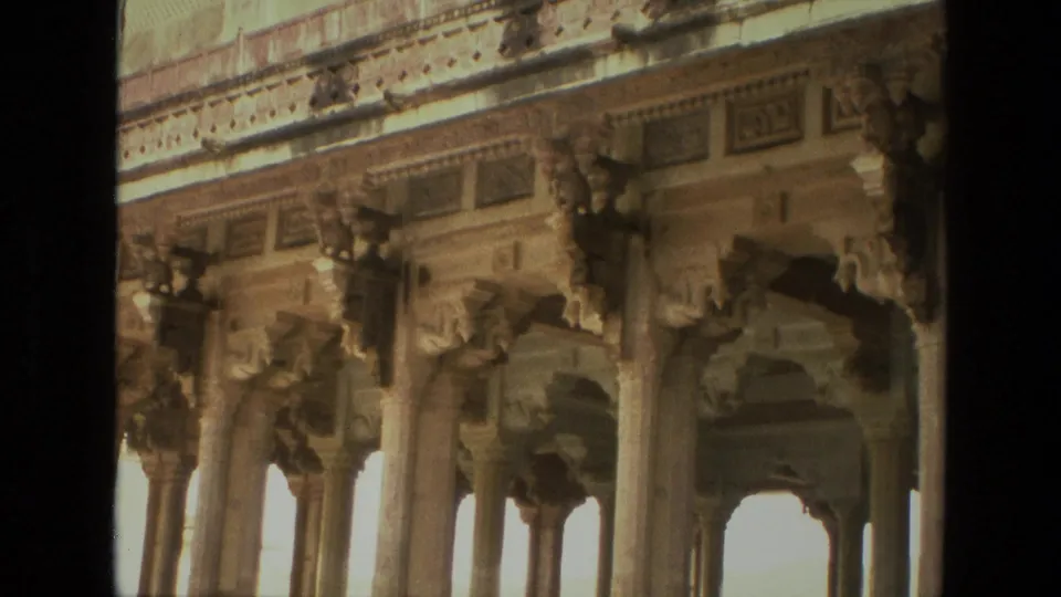 1974 India frame showing ornate carved stone columns, decorative brackets, a patterned frieze, and arched openings in historic architecture.