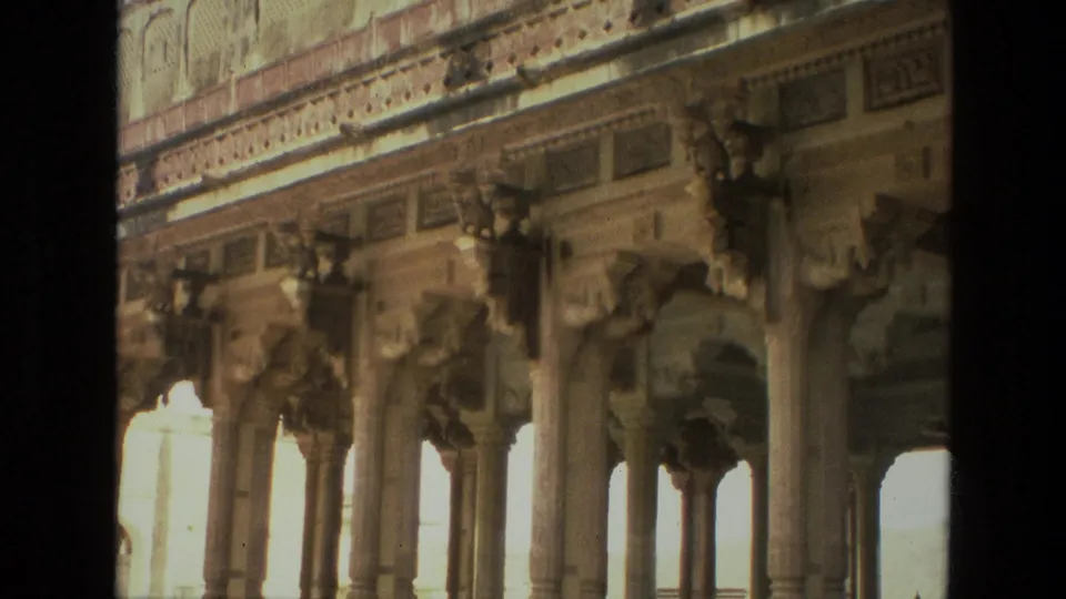 1974 India 8mm frame showing a historic colonnade with carved supports, arched openings, patterned stonework, and strong exterior light.