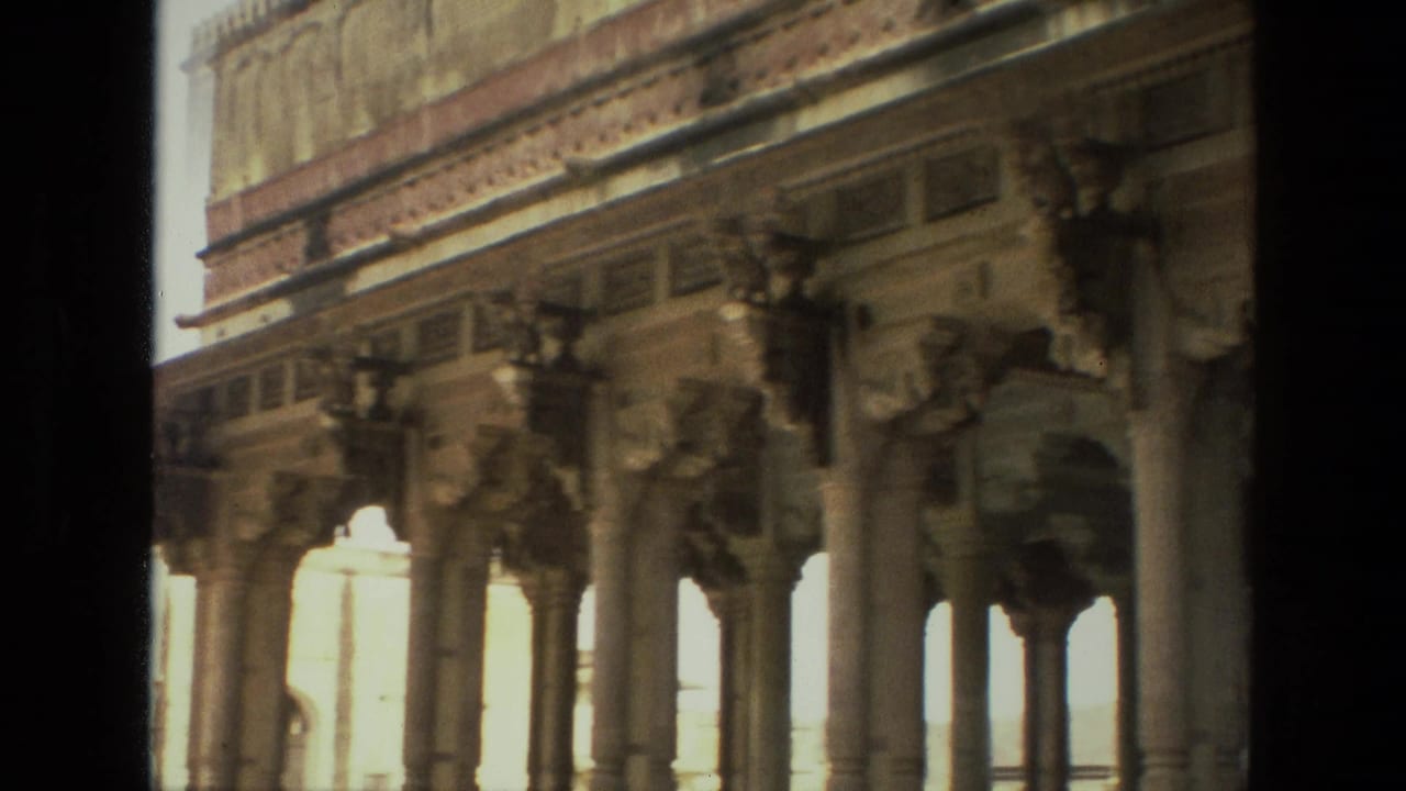 1974 India 8mm frame showing carved stone columns, bracket sculptures, and decorative frieze details viewed from a dark foreground edge.