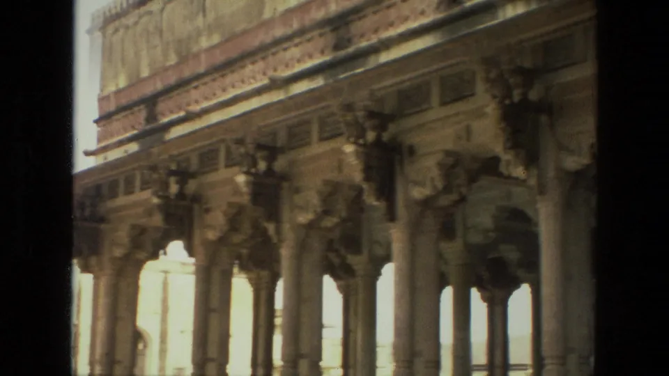 1974 India 8mm frame showing carved stone columns, bracket sculptures, and decorative frieze details viewed from a dark foreground edge.