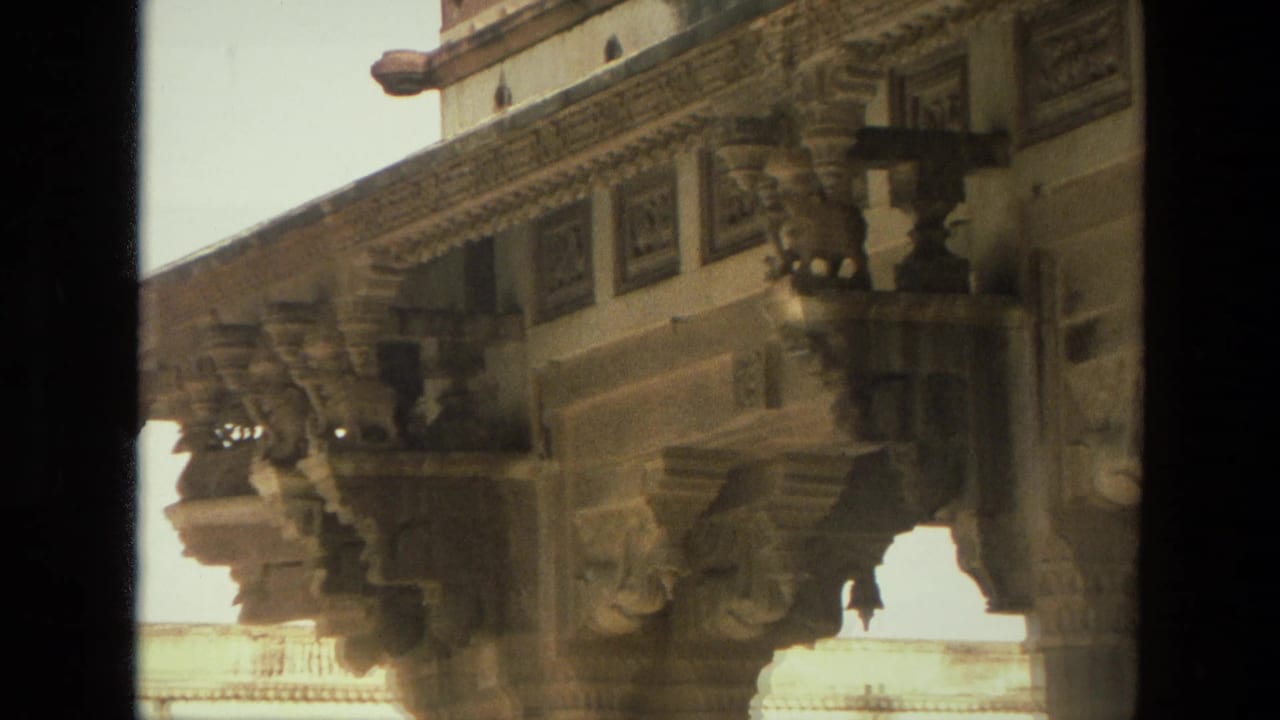 1974 India 8mm frame showing sculpted brackets and decorative stonework beneath a historic temple or palace overhang.