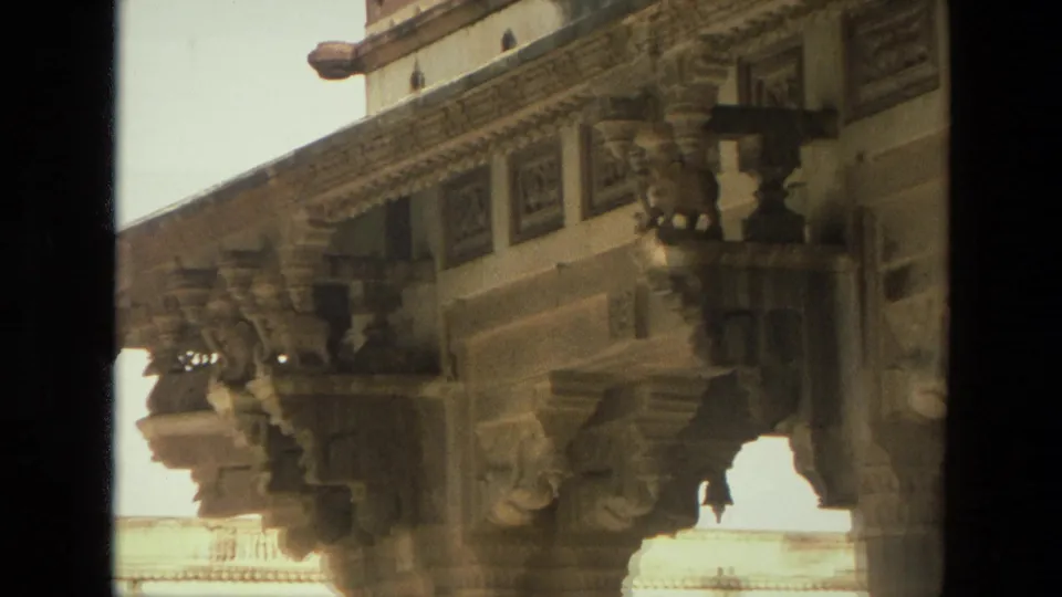 1974 India 8mm frame showing sculpted brackets and decorative stonework beneath a historic temple or palace overhang.