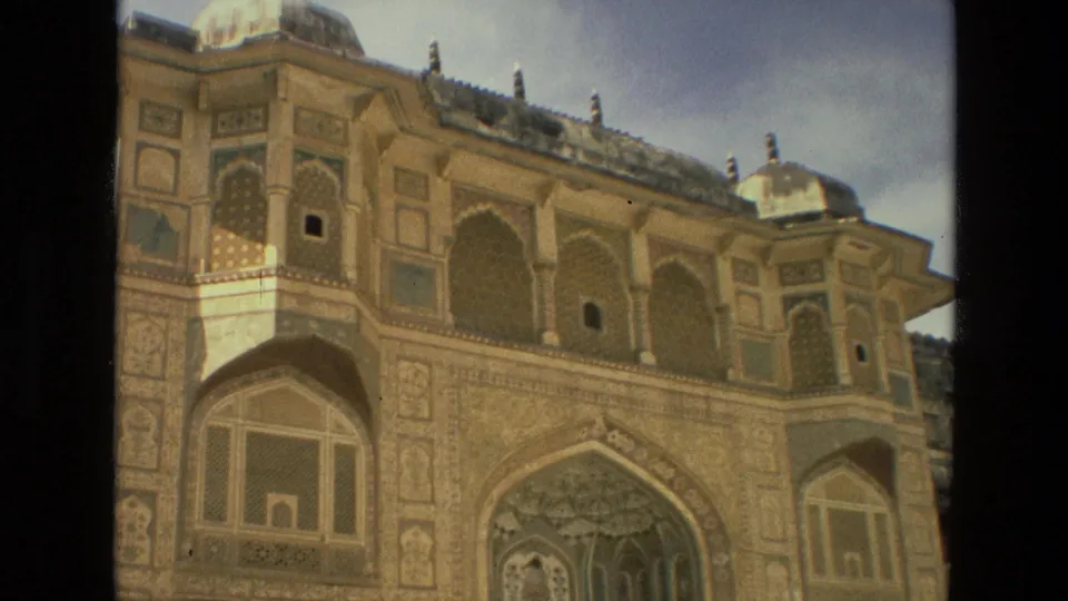 1974 India home-movie frame of an ornate historic facade with arched openings, geometric panels, and domed roof details.