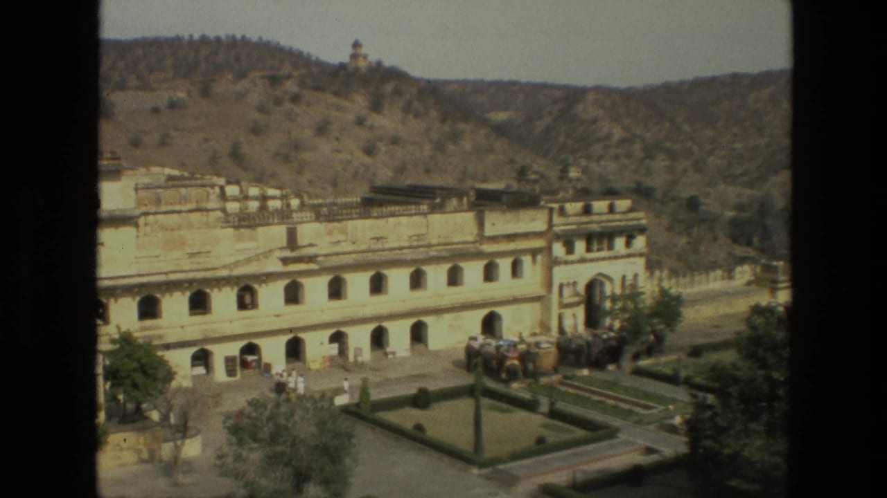 Palace entrance, courtyard garden, visitors, and elephants with hills behind the complex.