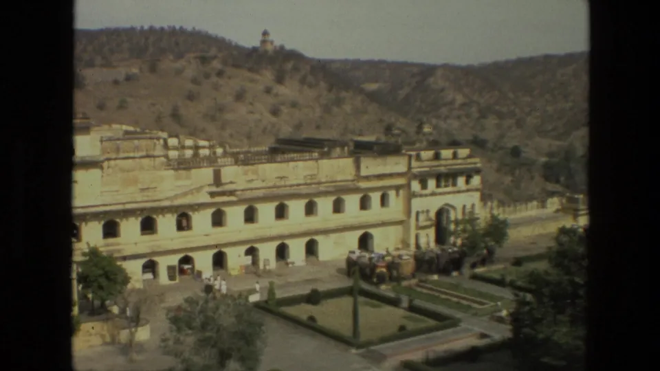 Elevated 1974 India home-movie view of a palace entrance, courtyard garden, visitors, elephants, and surrounding hills.