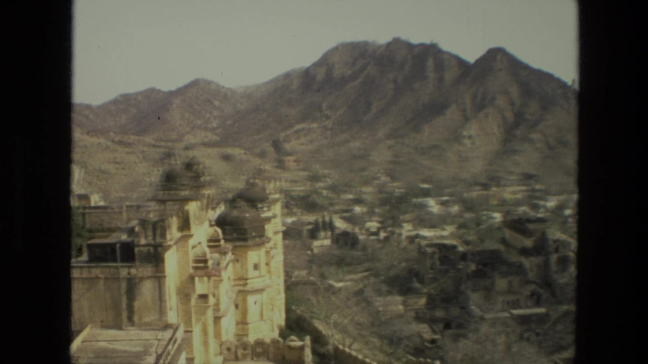 White domed buildings below rugged brown mountains in a hazy valley view.