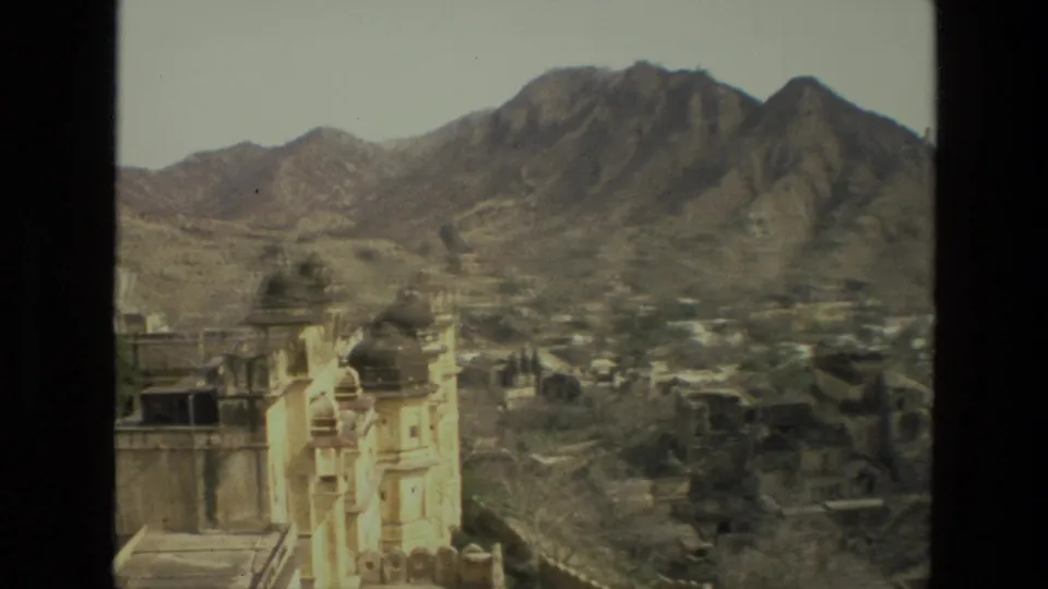 1974 India 8mm frame showing white domed architecture at the edge of a town below rugged brown mountain ridges.