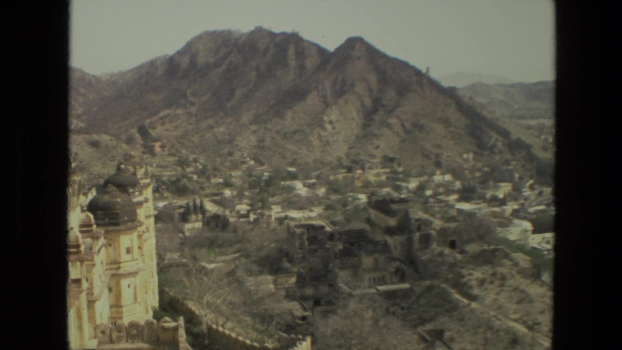 1974 India home-movie frame with a pale domed building in the foreground and a dense settlement under steep brown hills.