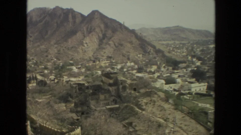 1974 India frame showing a wider valley settlement, white buildings, dry terrain, and a prominent rocky mountain slope.