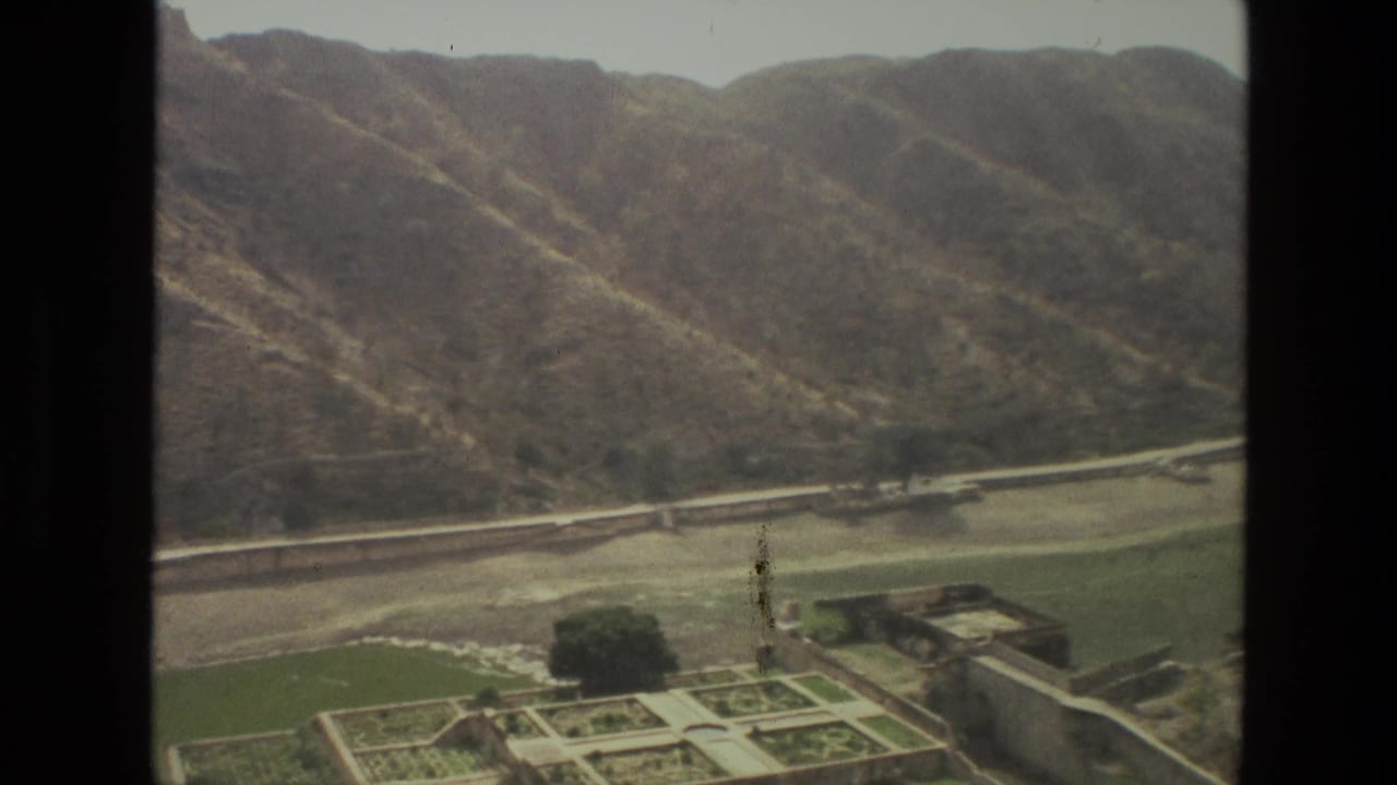 Aerial view of dry hills above a green valley with roads, plots, and dark window borders.
