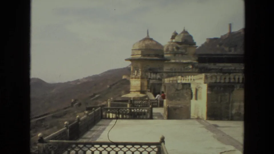 The pan settles on a hilltop palace or fort terrace in India, with visitors standing near domed architecture.