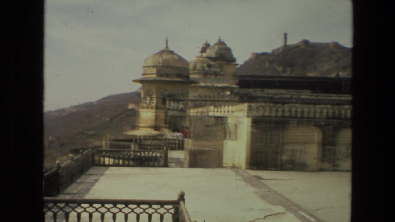 Domed palace structures and terrace railing beside a hillside under a hazy sky.