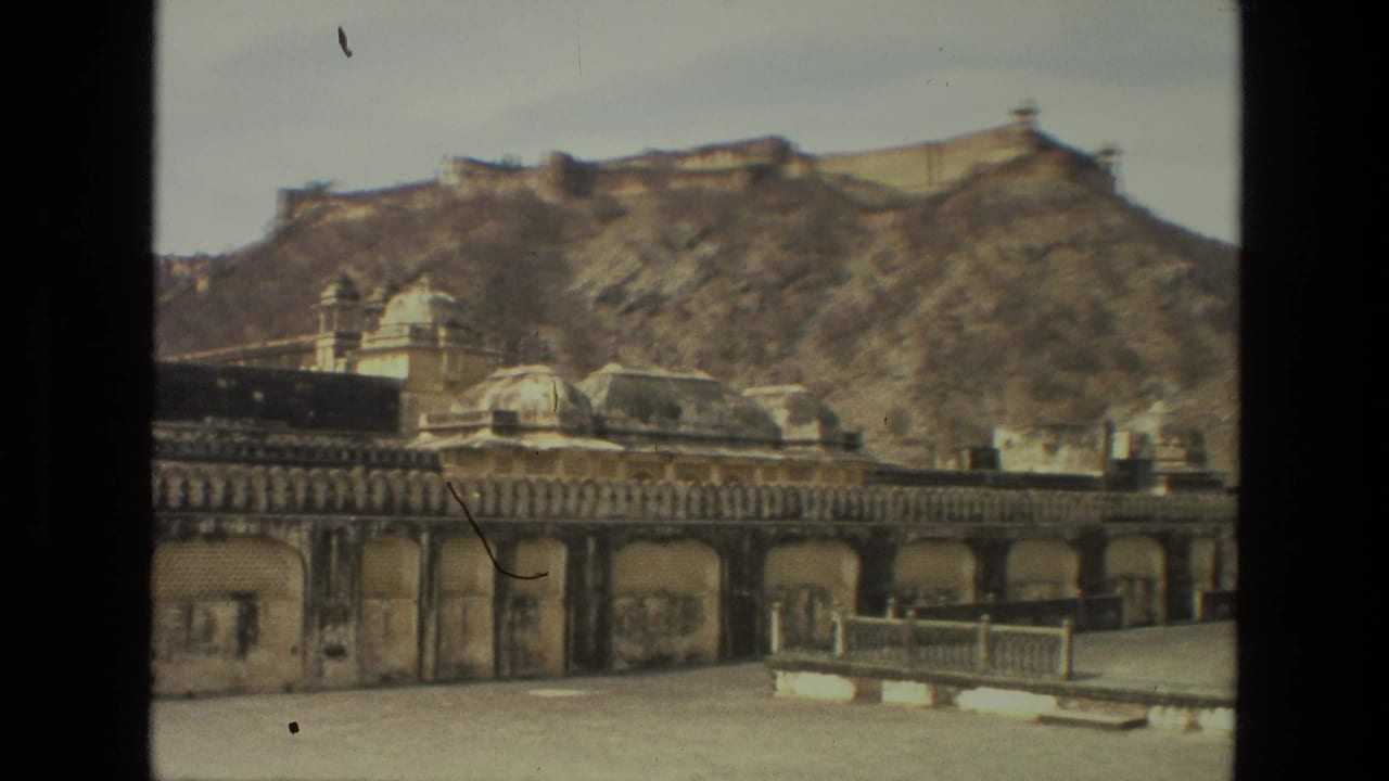 1974 India 8mm frame showing a weathered palace courtyard, arched stone facade, domed roofline, and a hilltop fort-like structure behind it.