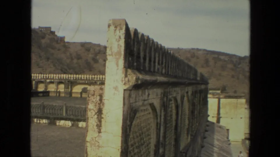 1974 India 8mm frame showing a weathered palace parapet and crenellated wall overlooking a hilly landscape.