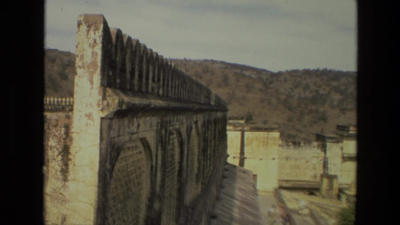 1974 India 8mm view along a crenellated palace wall with distant hills and pale architectural surfaces beyond.