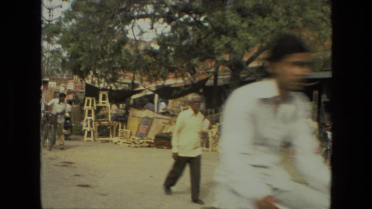 1974 8mm footage from India showing men walking and cycling past roadside wooden furniture stalls beneath trees.