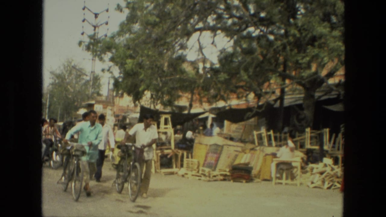 Several men ride bicycles past roadside wooden goods and shaded market stalls.