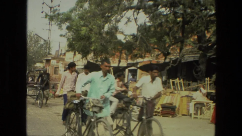 1974 India street scene with cyclists in the foreground, a horse-drawn cart at left, and wooden market goods along the road.