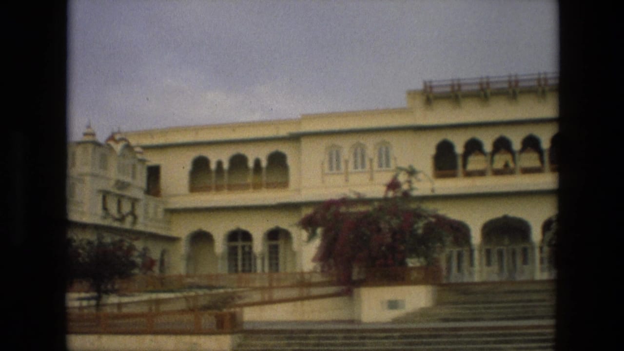 Palace exterior with arched openings, steps, railings, and flowering plants in front.