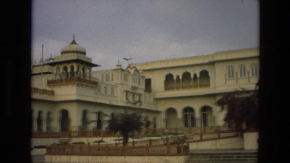 1974 India home-movie frame showing a palace corner with a domed turret, arched lower openings, railings, and steps.
