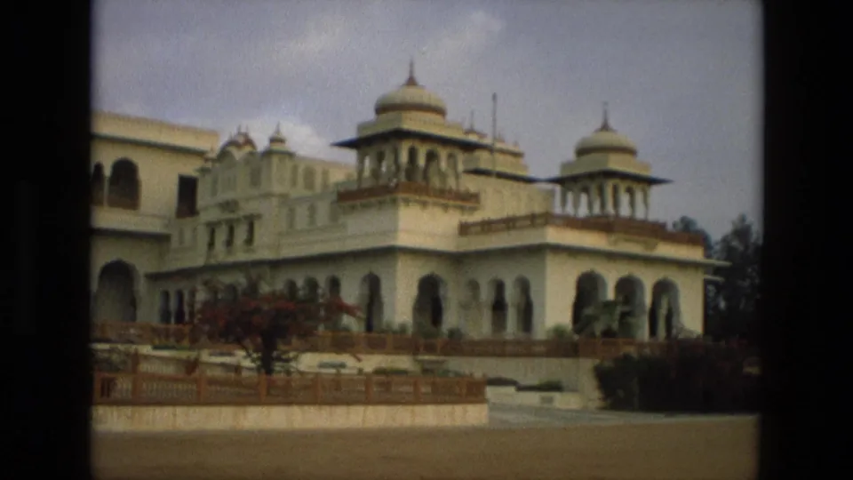 1974 India 8mm frame of a palace or heritage building wing with domed chhatris, arched windows, terrace railings, and open grounds.