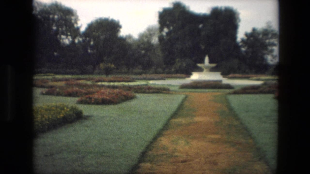 Formal garden path leading toward a white central fountain surrounded by lawns and trees.