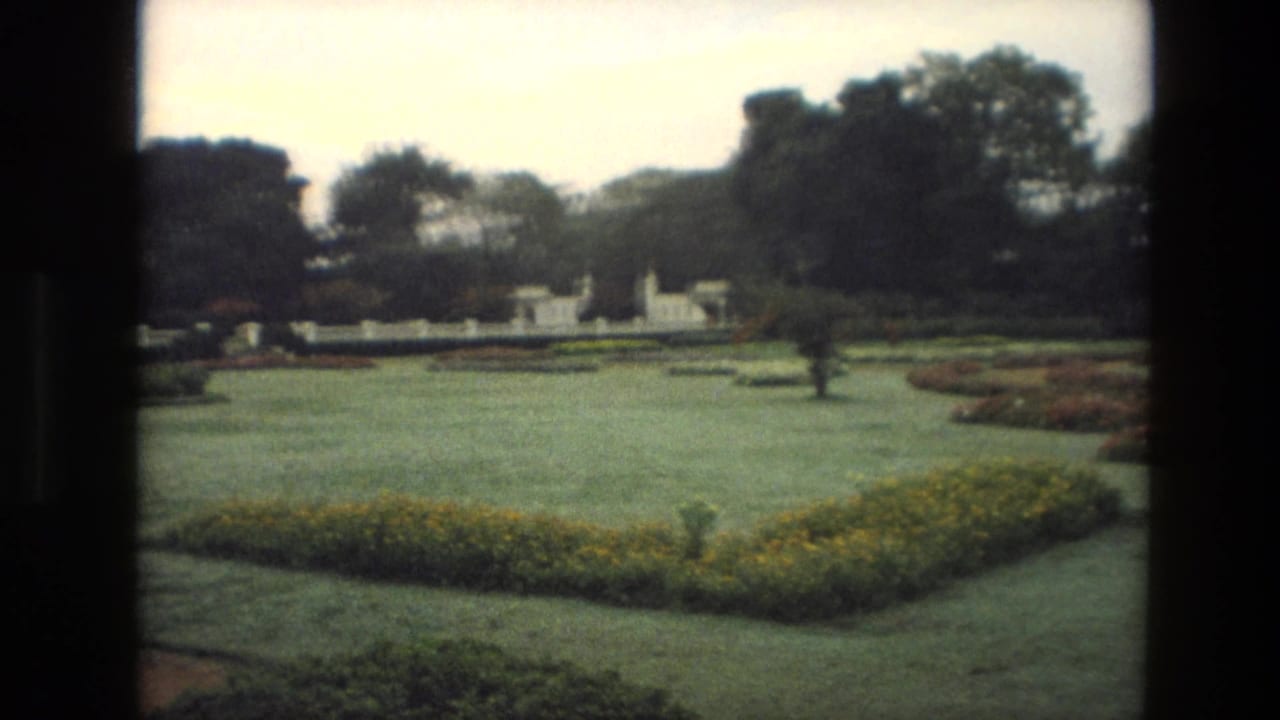 Formal garden lawn with flowerbeds, white wall, and trees under an overcast sky.
