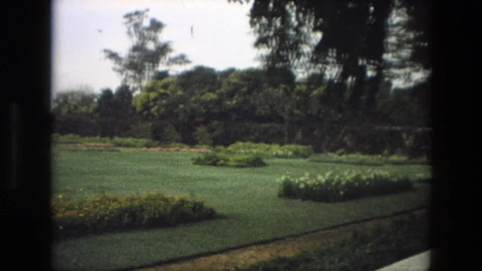 1974 India 8mm frame showing a formal garden with lawn, flowerbeds, dense trees and soft, warm film color.