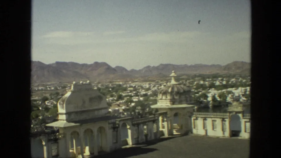 1974 India 8mm panorama from an elevated terrace, showing white domed architecture, town rooftops and distant mountains.