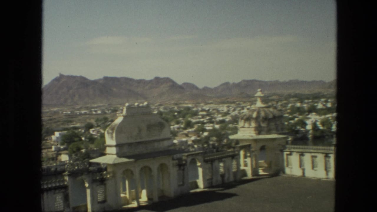 Elevated view over white domed architecture, town buildings, trees, and distant mountains.