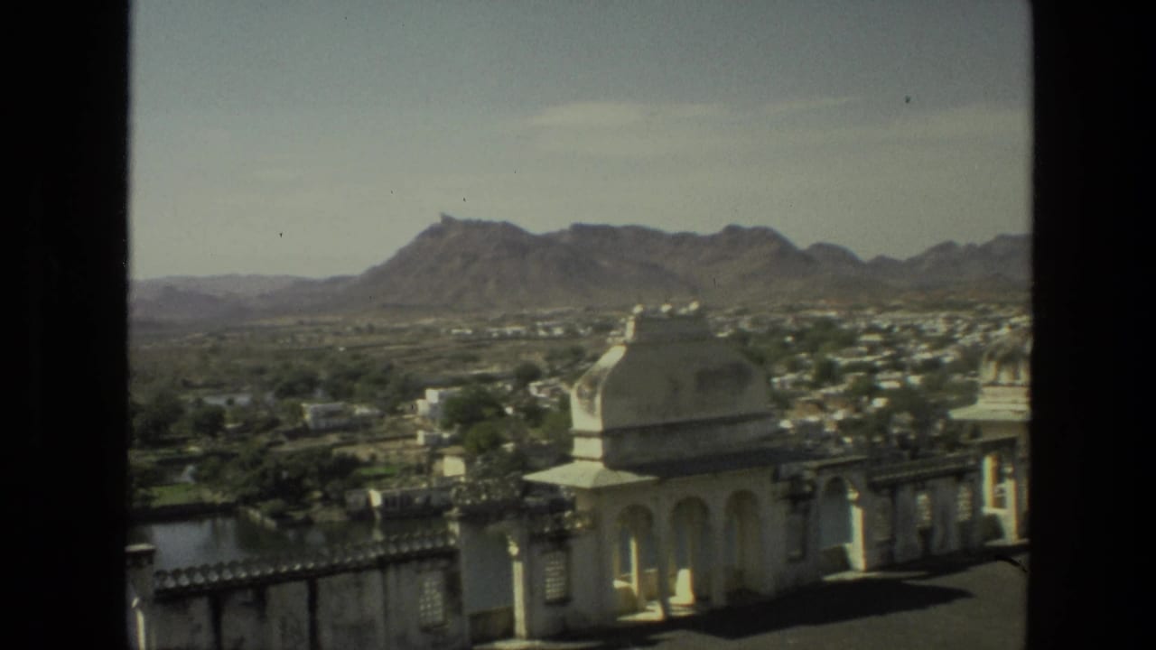 1974 India frame with a white domed pavilion at right, terrace architecture below, and hazy hills beyond the town.