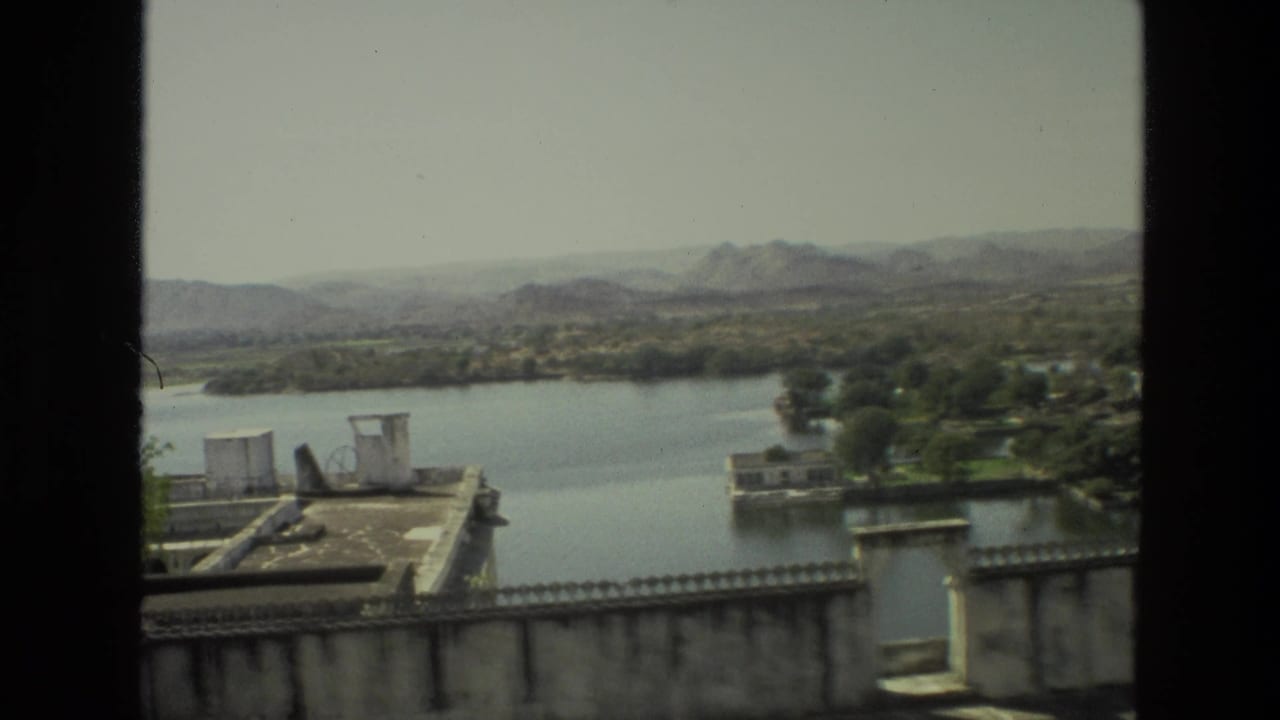 Elevated lake view with stone parapet, rooftop structures, trees, and hazy hills beyond the water.