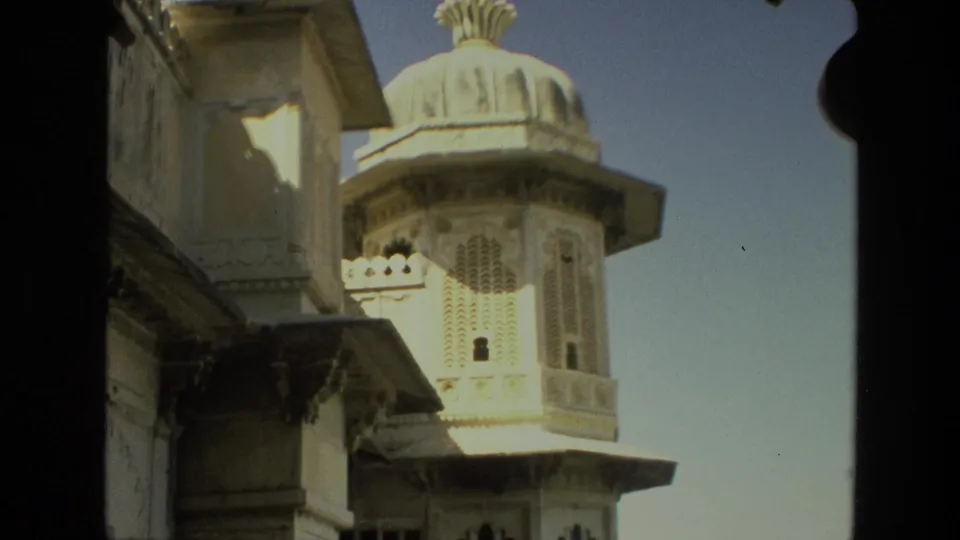 1974 India 8mm frame of an ornate pale stone palace tower with a domed roof, partly framed by dark architectural shadows.