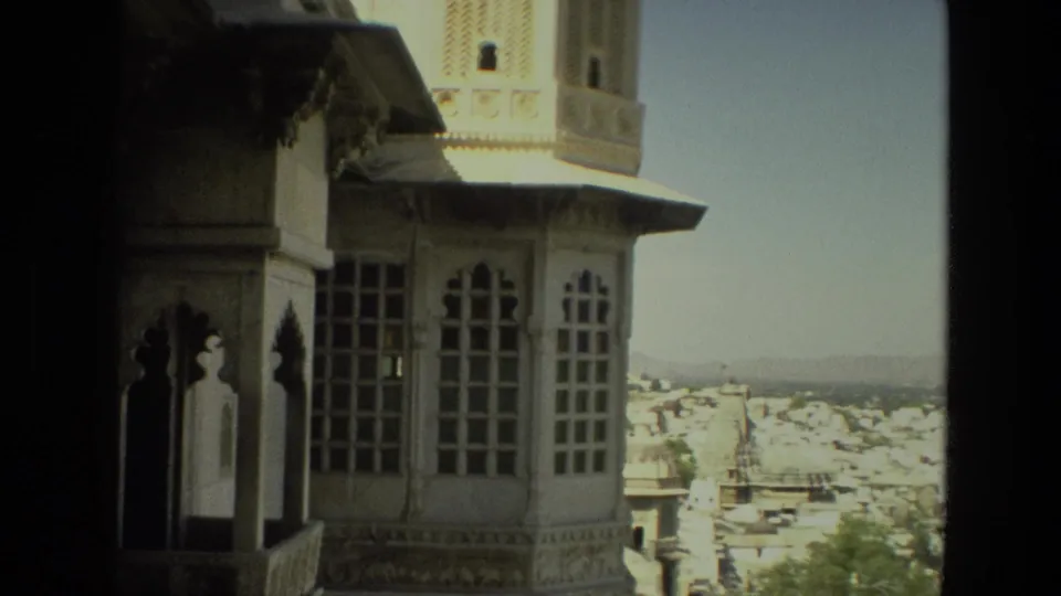 1974 India 8mm footage frames a palace tower and arched windows against a broad view of dense white city buildings and distant hills.
