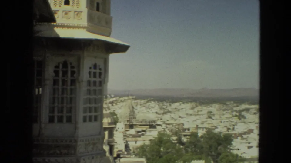 The final 1974 India frame shows the palace facade at left and a sunlit city panorama stretching toward low hills beneath a clear sky.