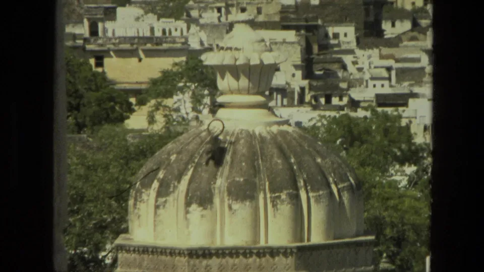 1974 India 8mm frame showing the monkey descending across a pale ribbed dome, with trees and clustered buildings in the background.