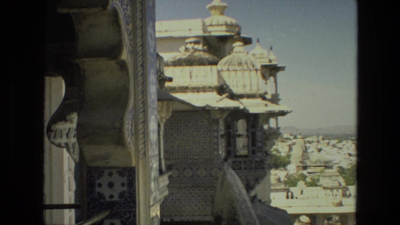 Ornate tiled wall, projecting balcony, domes, and distant city buildings under bright sky.